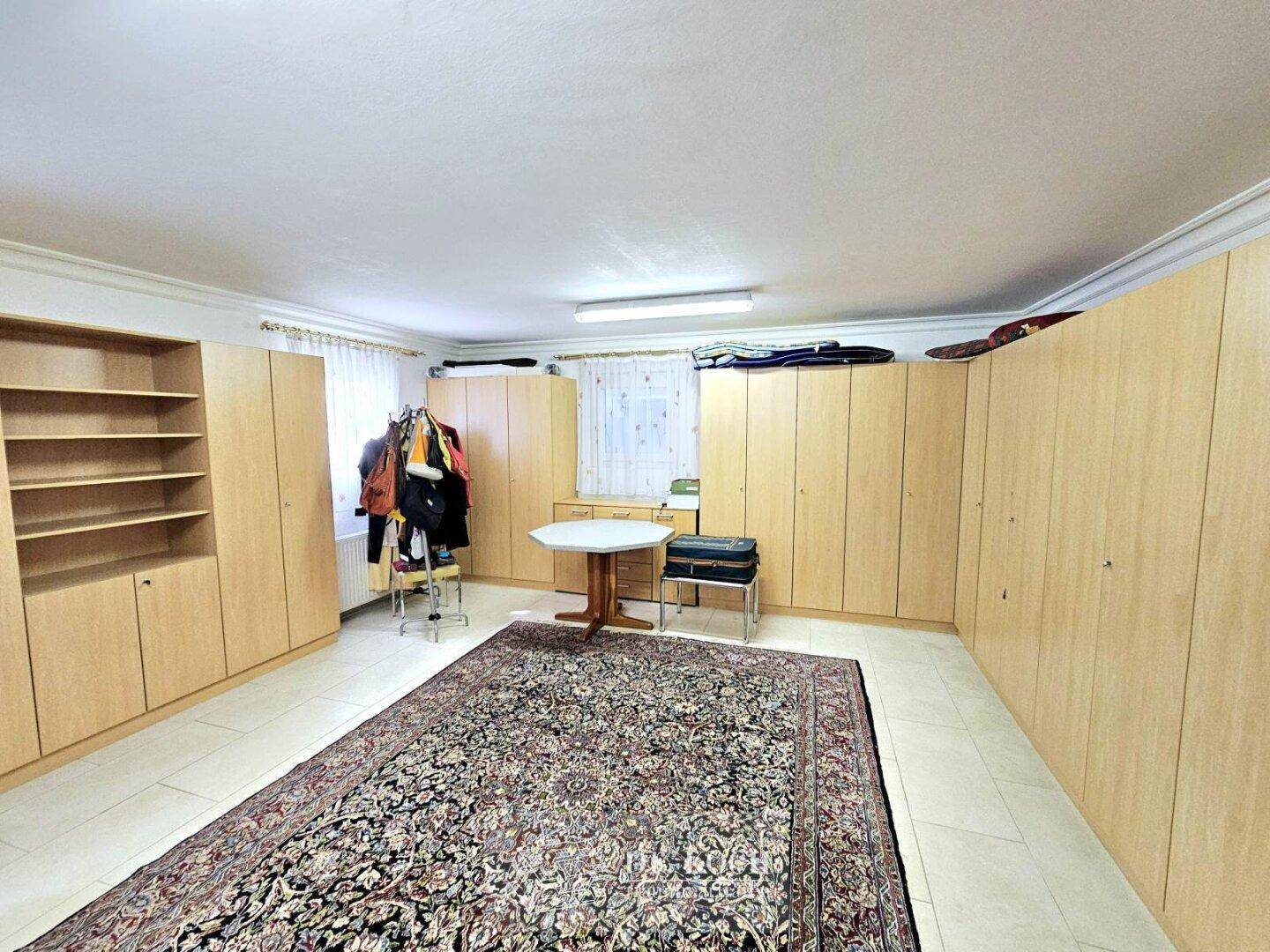 Großer Abstellraum mit vielen Holzschränken und einem Teppich auf dem Fliesenboden.