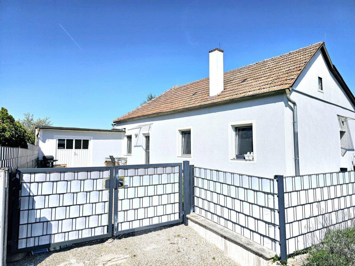 Weißes Einfamilienhaus mit Satteldach und Metallzaun im Vorgarten.