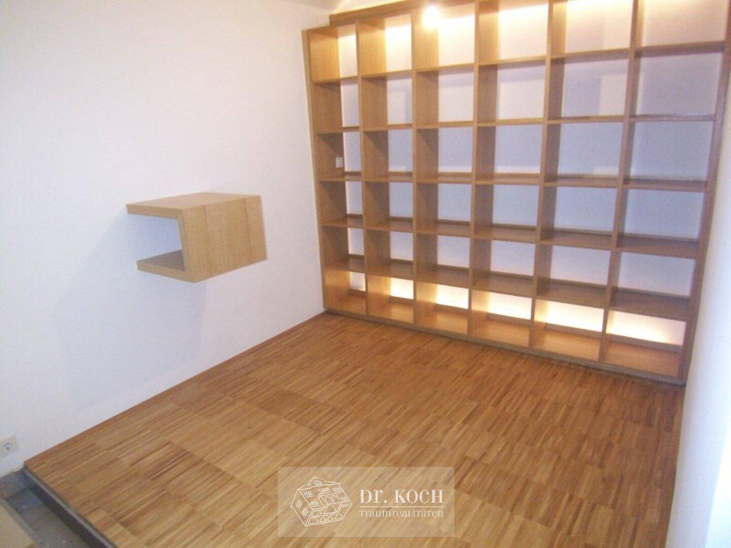 Heller Raum mit Holzparkettboden und integriertem Bücherregal, ideal als Büro oder Ankleidezimmer.