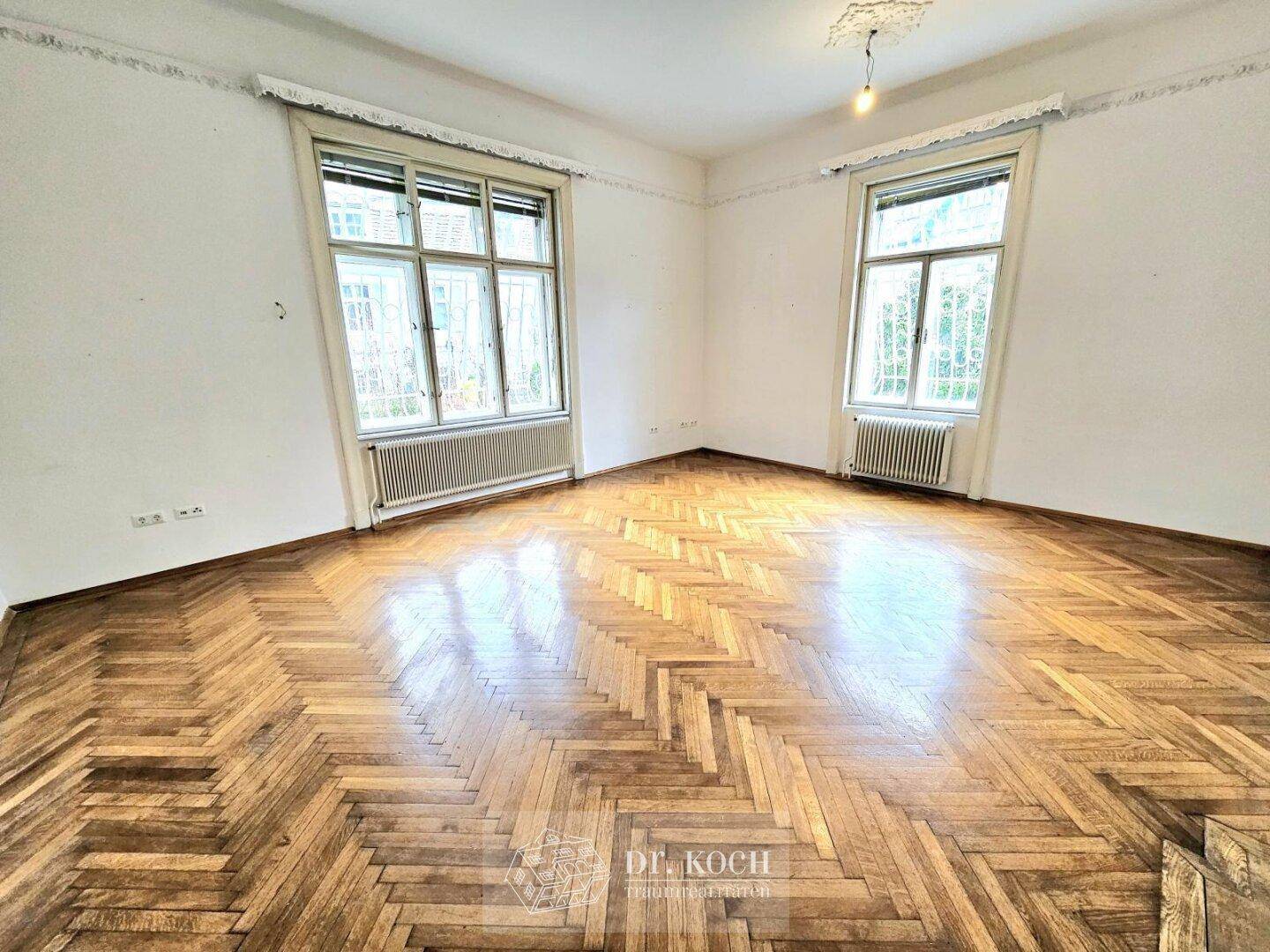 Geräumiges Zimmer mit Fischgrätparkett und großen Fenstern, bereit zur individuellen Gestaltung.