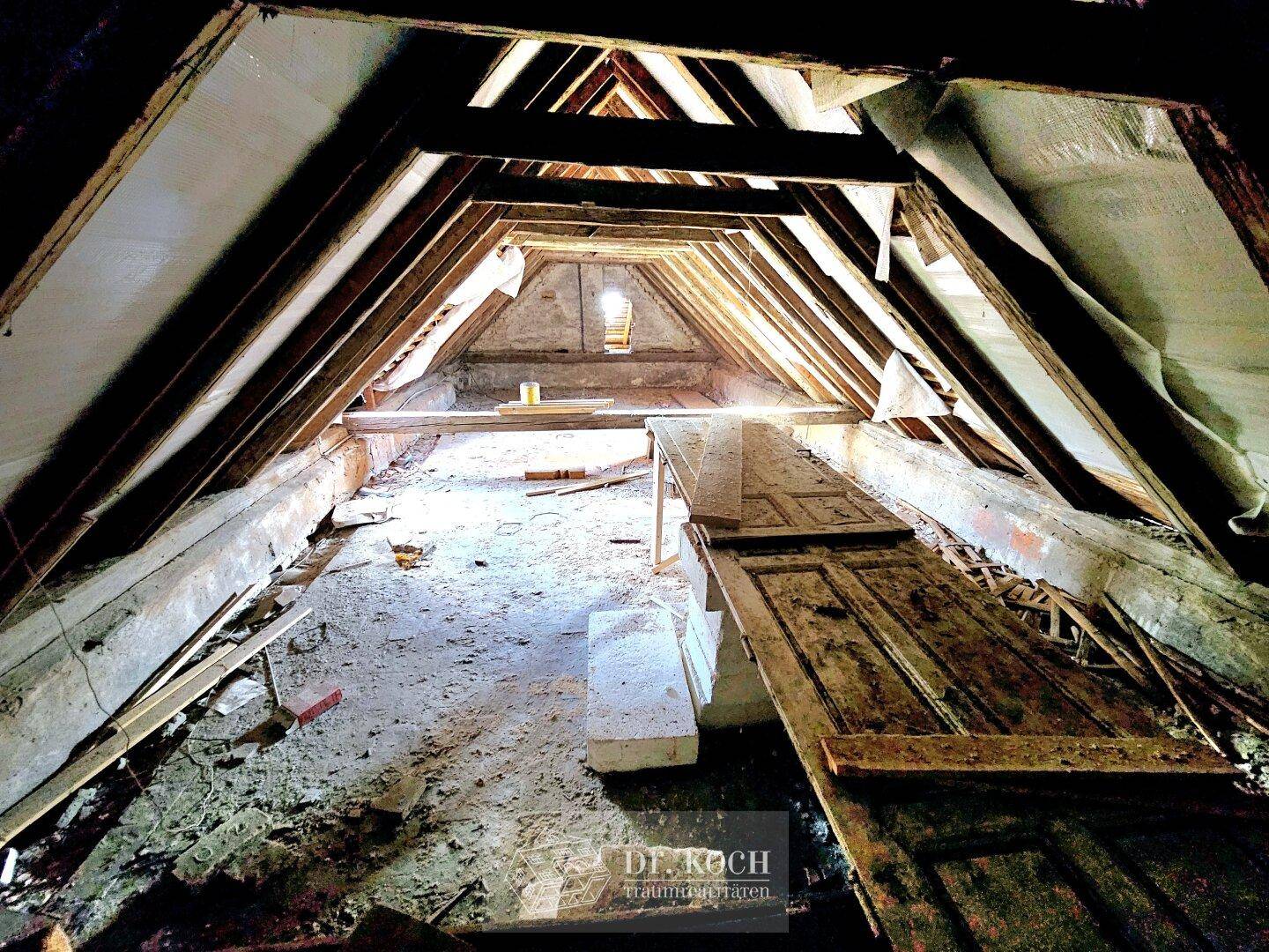 Langer, schmaler Dachbodenraum mit freiliegenden Holzbalken und natürlichem Lichteinfall.