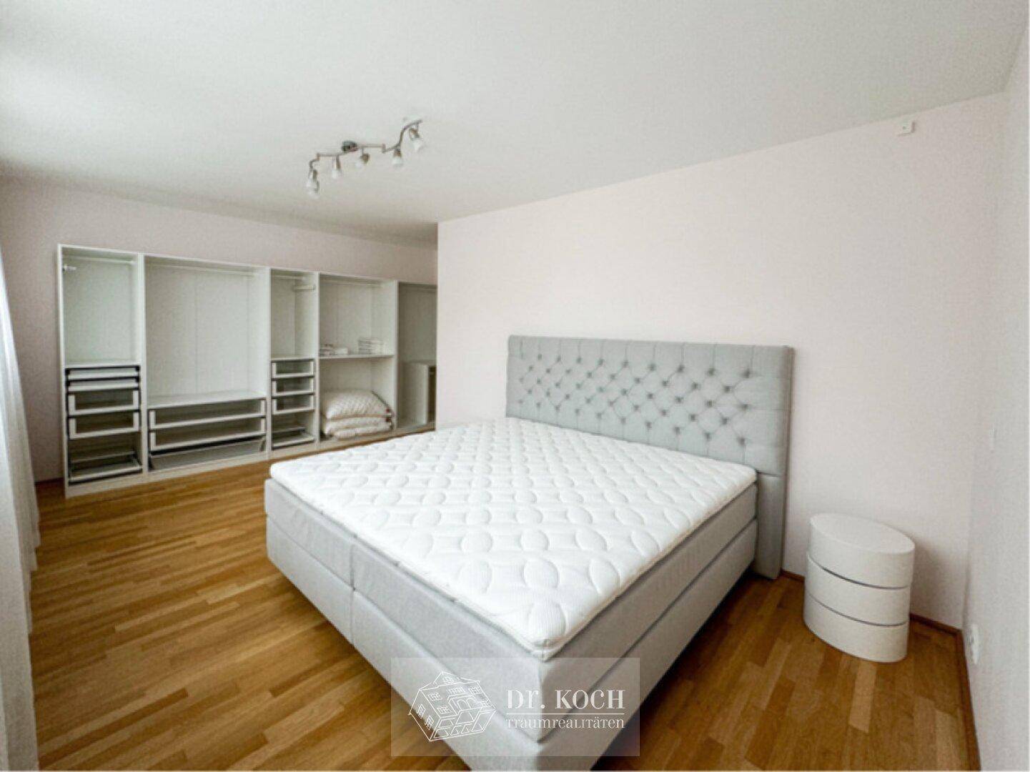 Schlafzimmer mit Holzboden, offenem Schranksystem und großem, komfortablem Bett.