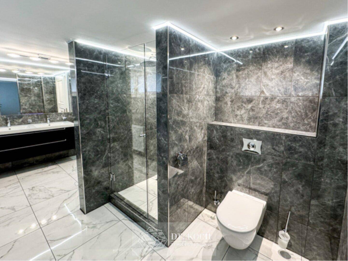 Luxuriöses Badezimmer mit dunklen Marmorfliesen, begehbarer Dusche und Doppelwaschbecken.