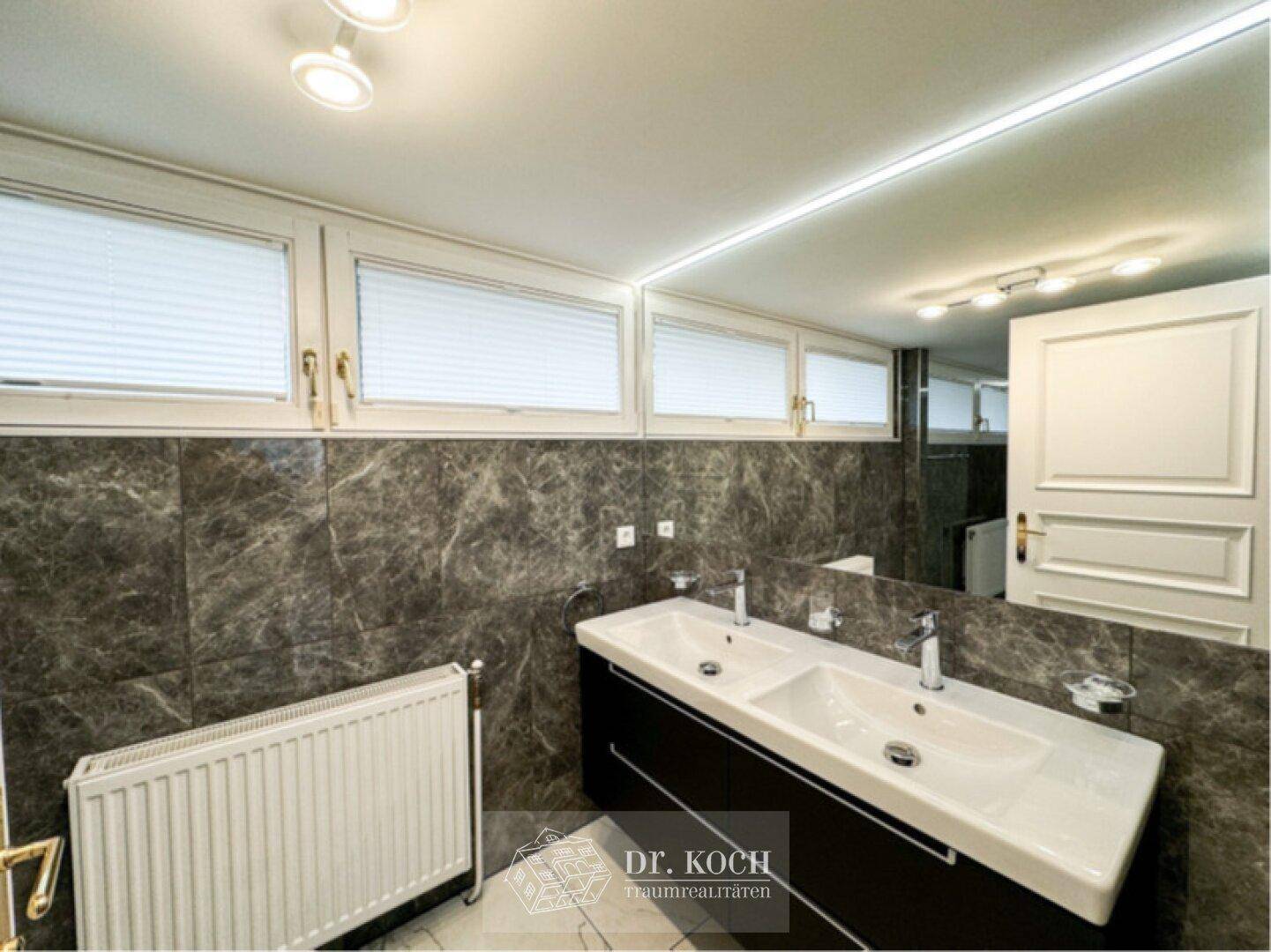 Modernes Badezimmer mit Doppelwaschbecken, großem Spiegel und dunklen Marmorfliesen.