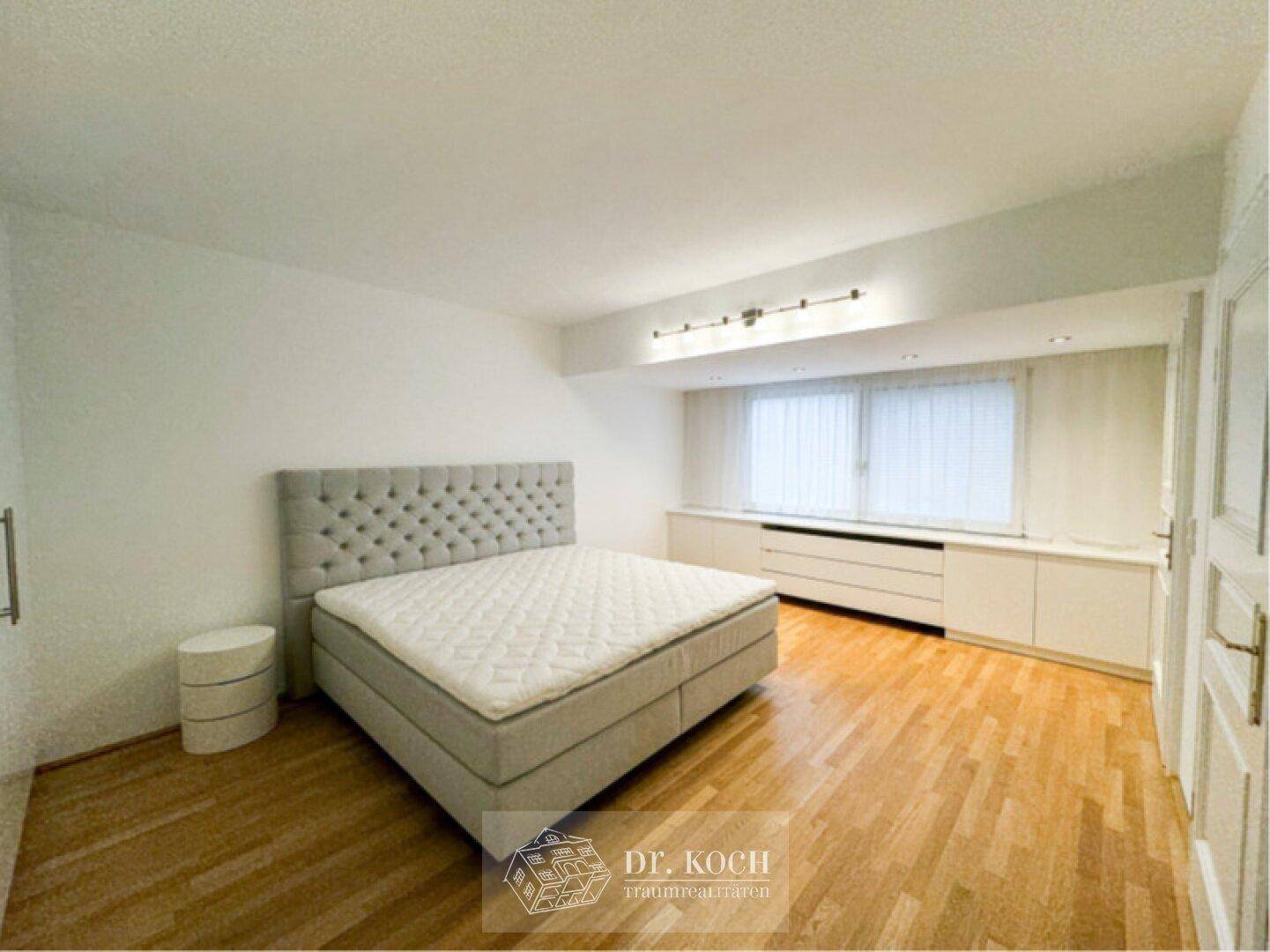 Schlafzimmer mit Holzboden, großem Bett und integrierten Schränken unter dem Fenster.