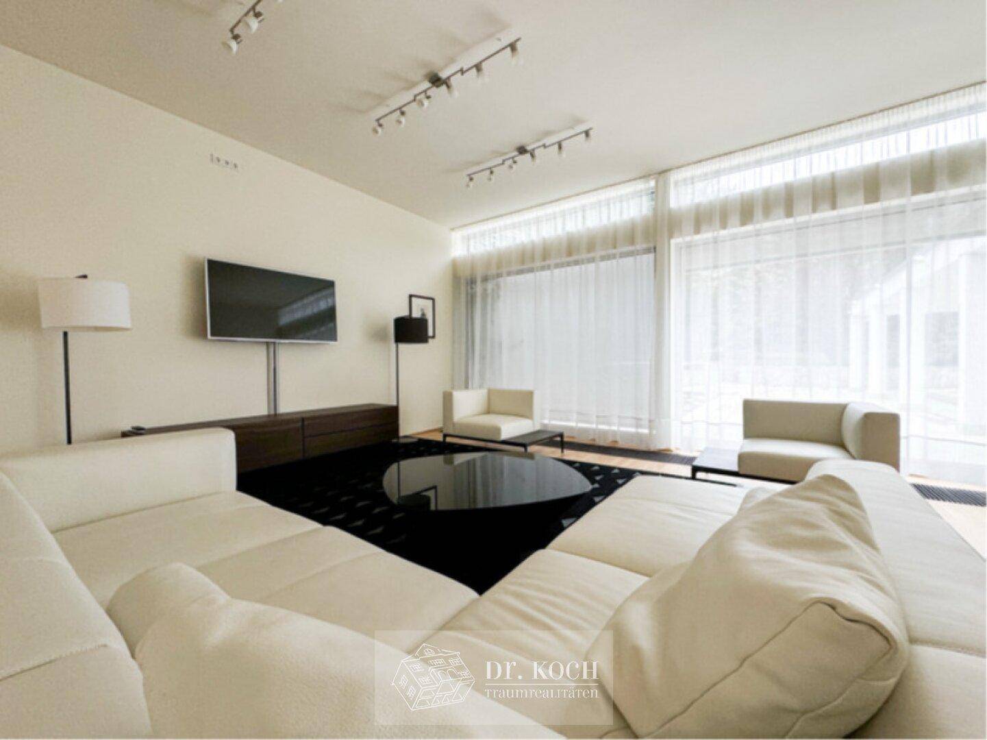 Heller Wohnbereich mit modernem Sofa, Couchtisch und großen Fenstern mit Vorhängen.