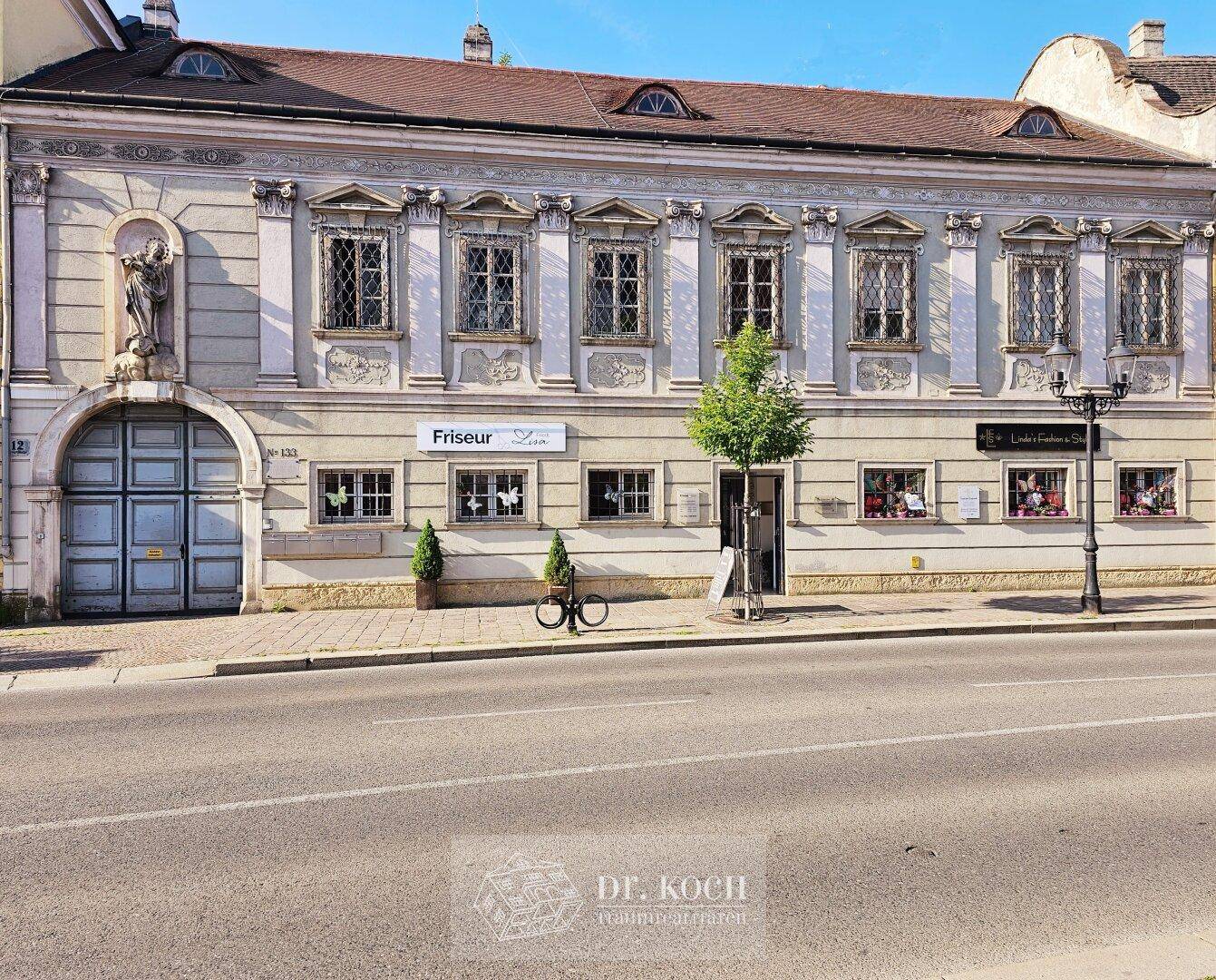 Historisches Gebäude mit aufwendiger Fassade, großen Fenstern und Geschäftsflächen im Erdgeschoss.