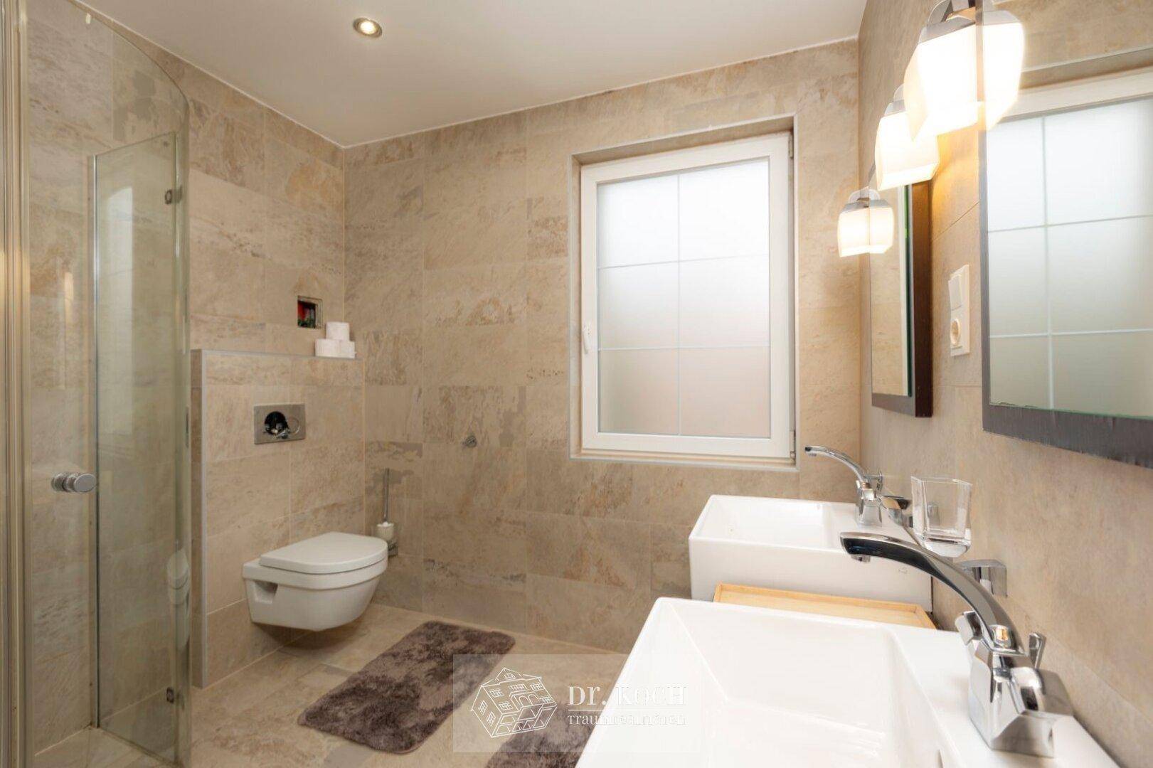 Modernes Badezimmer mit Doppelwaschbecken, Dusche und Fenster für angenehmes Tageslicht.
