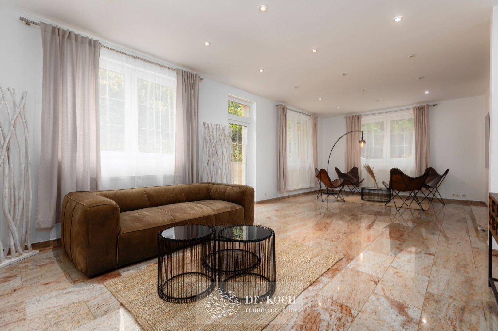 Geräumiges Wohnzimmer mit modernem Sofa, glänzendem Marmorboden und viel Tageslicht.