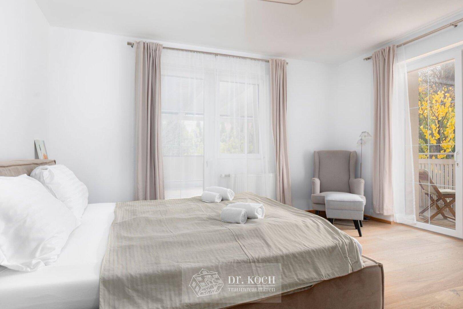Helles Schlafzimmer mit gemütlichem Sessel und Zugang zu einem sonnigen Balkon, ideal zum Entspannen.