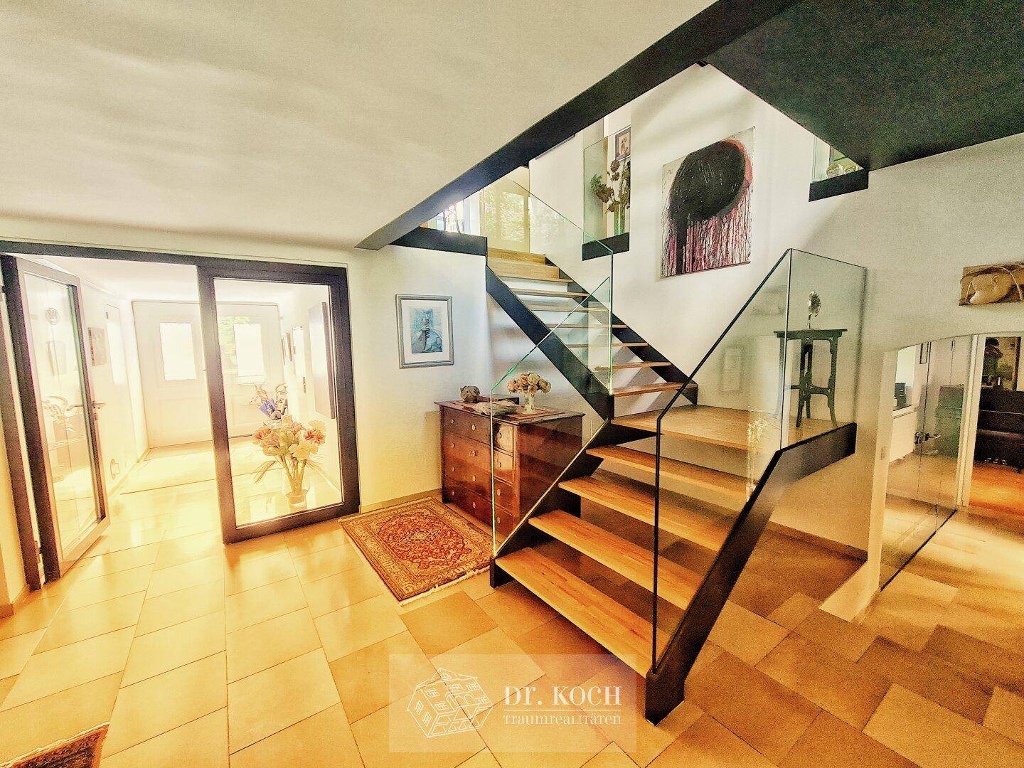 Moderner Eingangsbereich mit eleganter Holztreppe, Glasgeländer und Fliesenboden.