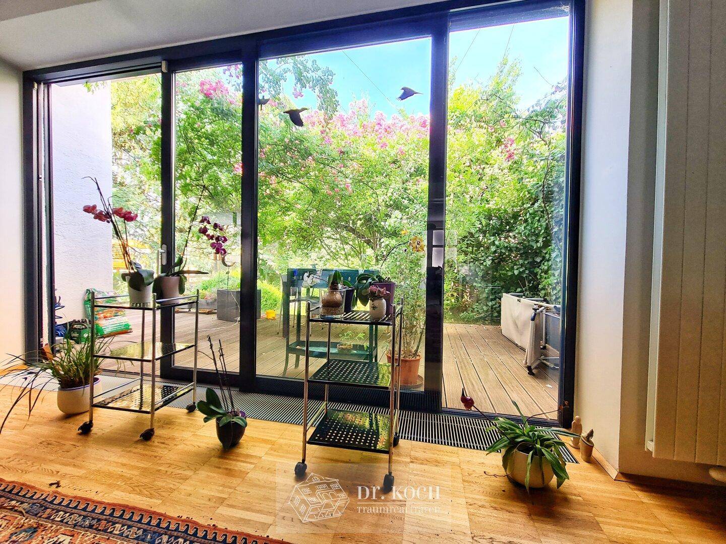 Heller Innenraum mit großen Schiebetüren, die den Blick auf die Holzterrasse und den grünen Garten freigeben.