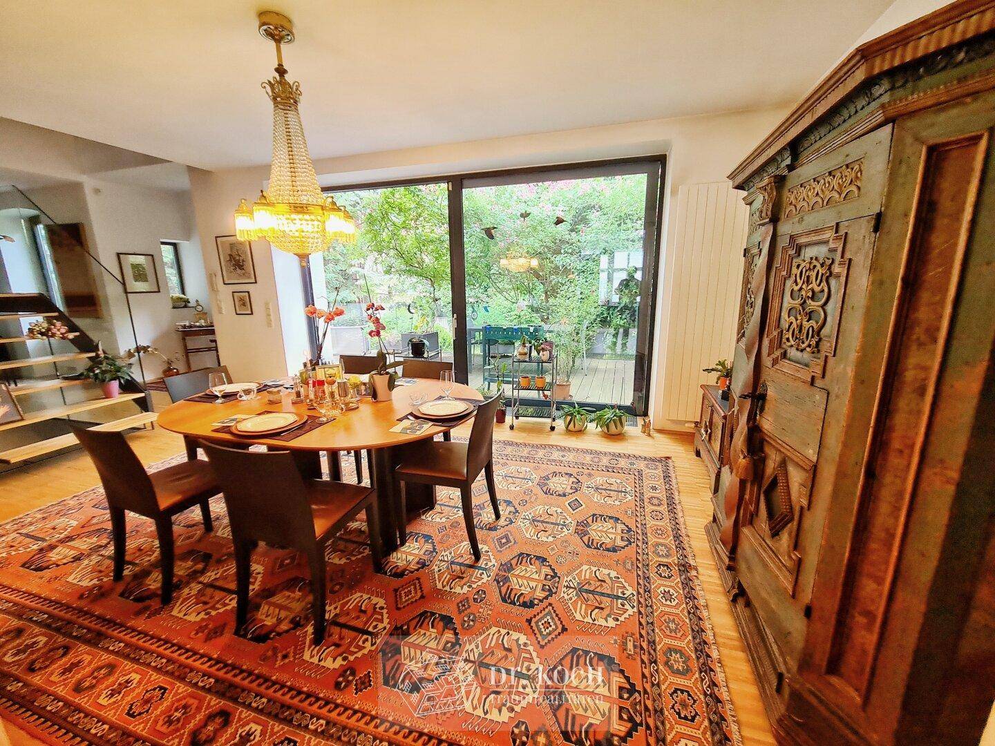 Eleganter Essbereich mit großem Holztisch, orientalischem Teppich und einem antiken Schrank mit Gartenblick.