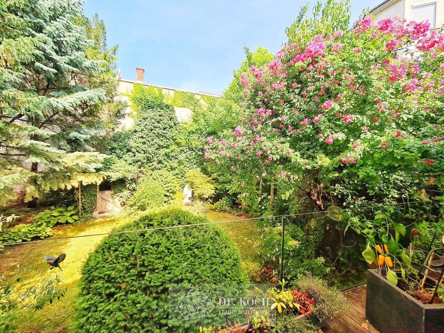 Üppiger Garten mit vielfältiger Bepflanzung, blühenden Sträuchern und einem kleinen Gartenhaus.