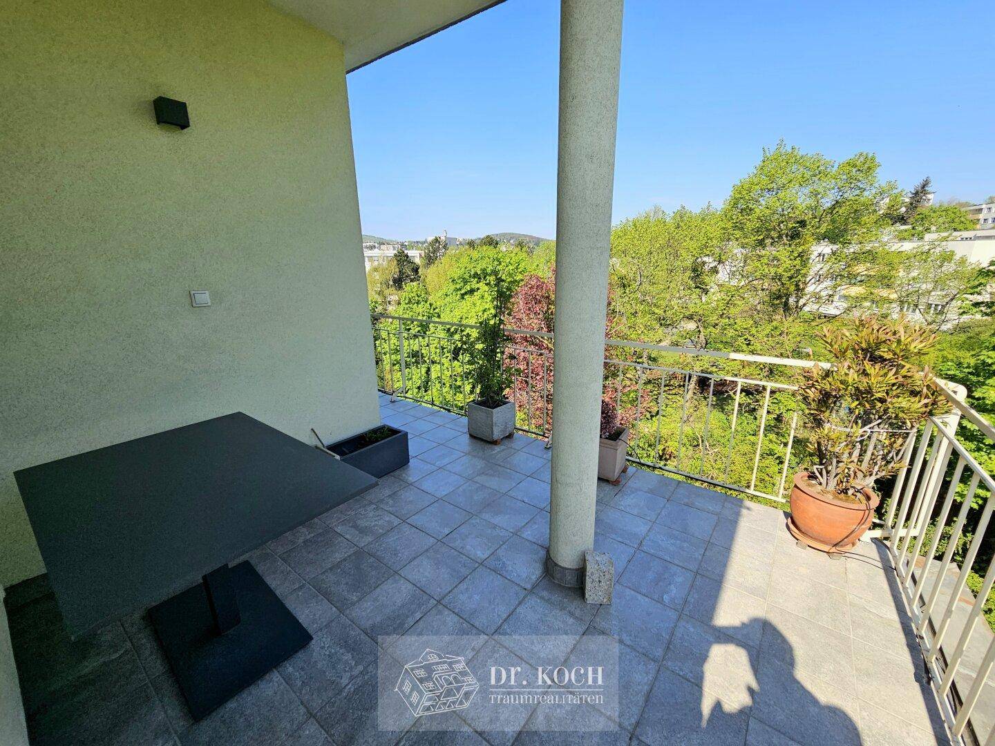 Geflieste Terrasse mit einem Tisch, Stühlen und Topfpflanzen, umgeben von viel Grün.