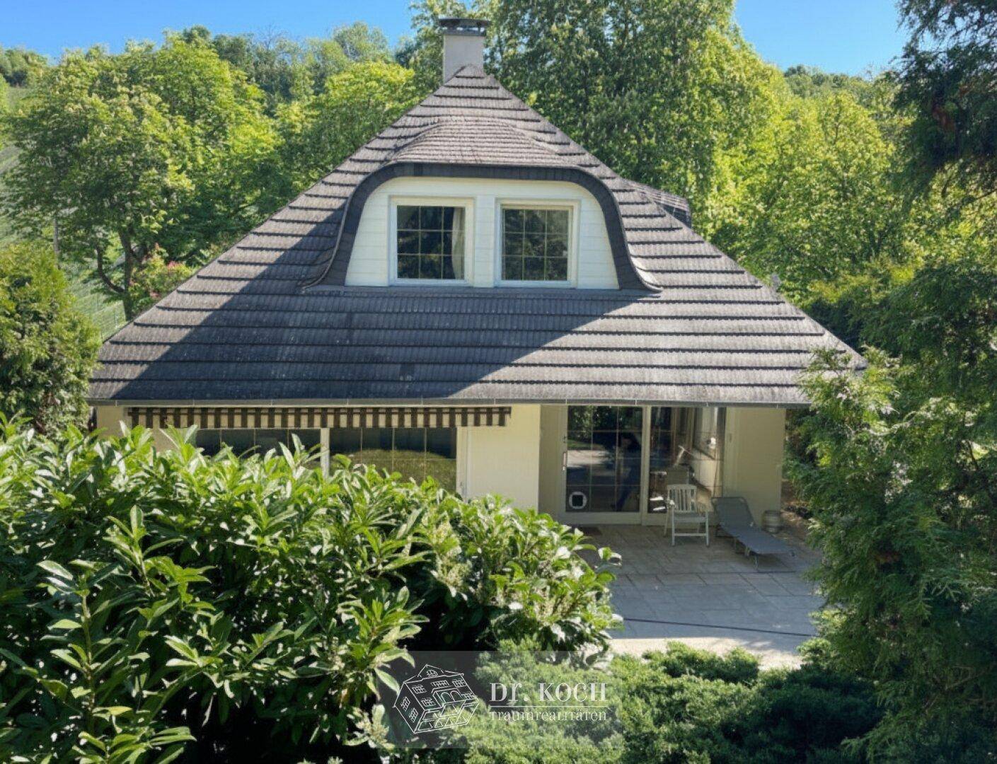 Rückseite des Hauses mit großer Terrasse, Markise und Blick in den grünen Garten.