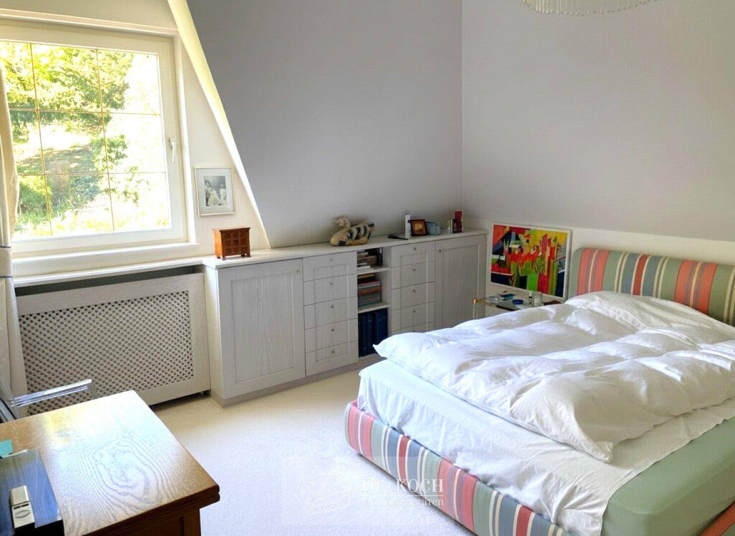 Helles Schlafzimmer im Dachgeschoss mit schrägen Wänden, Einbauschränken und Fenster.