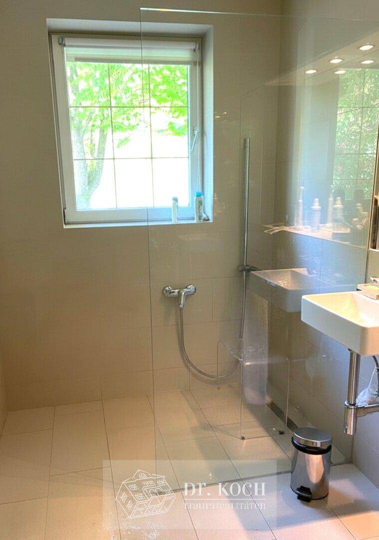Modernes Badezimmer mit ebenerdiger Dusche, Fenster und hellem Fliesenboden.
