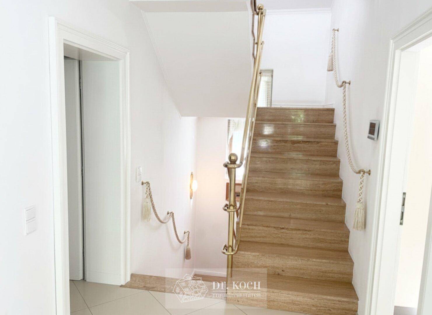 Elegantes Treppenhaus mit Marmorstufen und goldenem Geländer, führt in die oberen Etagen.