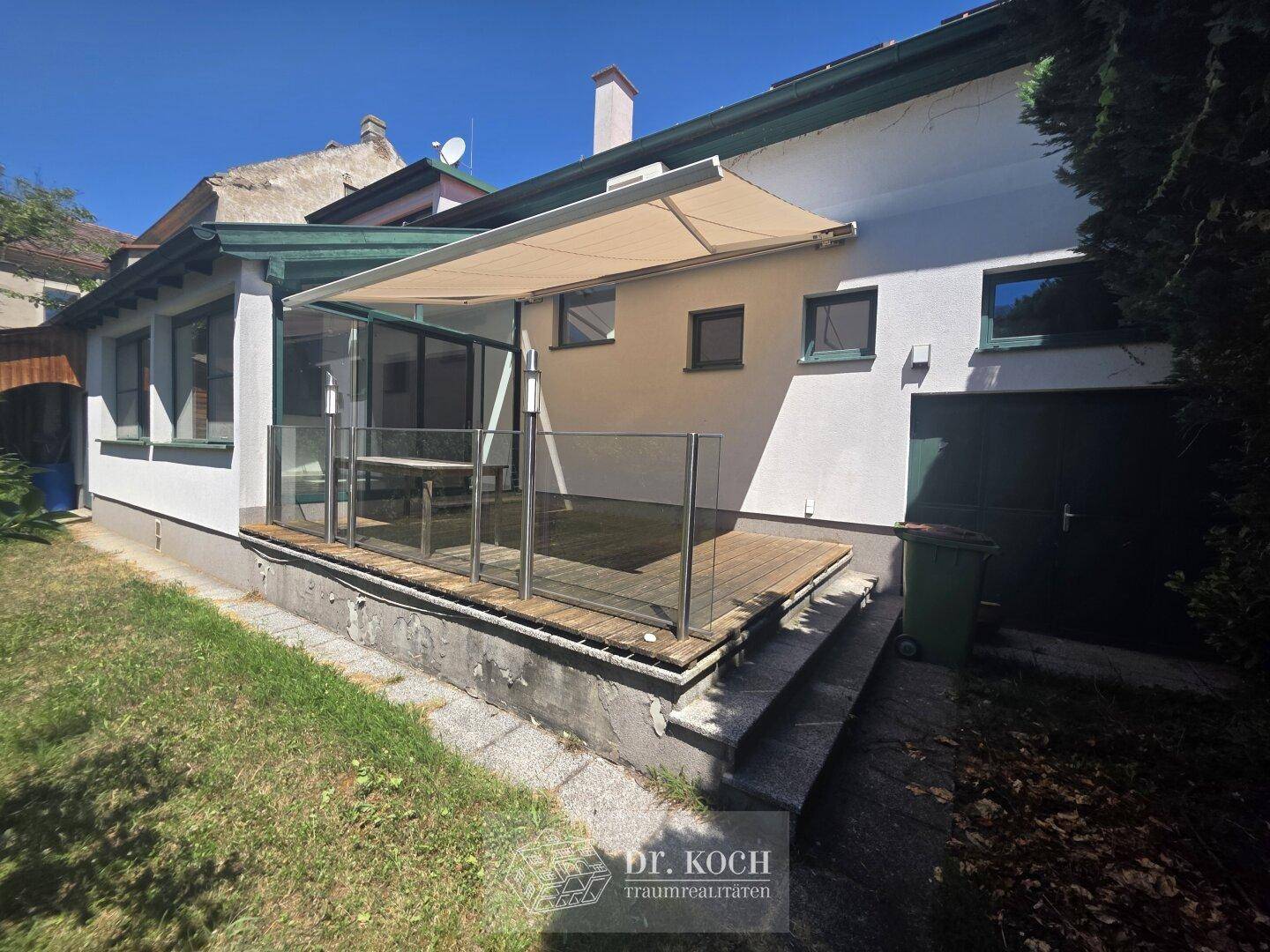 Sonnenterrasse mit Markise, Glasgeländer und Holzboden, ideal für entspannte Stunden im Freien.