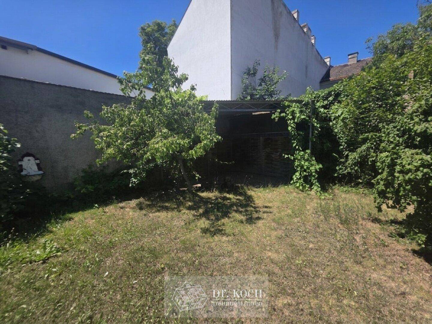 Hinterer Gartenbereich mit Rasen, Bäumen und einem überdachten Unterstand.