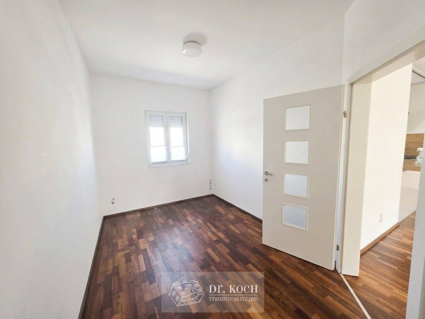 Helles, leeres Zimmer mit Parkettboden und Fenster, ideal als Schlaf- oder Arbeitszimmer.