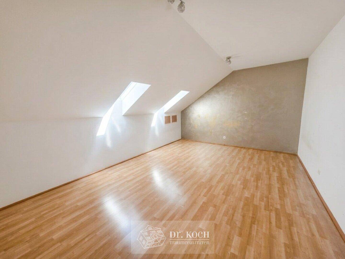 Helles Dachzimmer mit Holzboden, schrägen Wänden und zwei Dachfenstern für viel Licht.