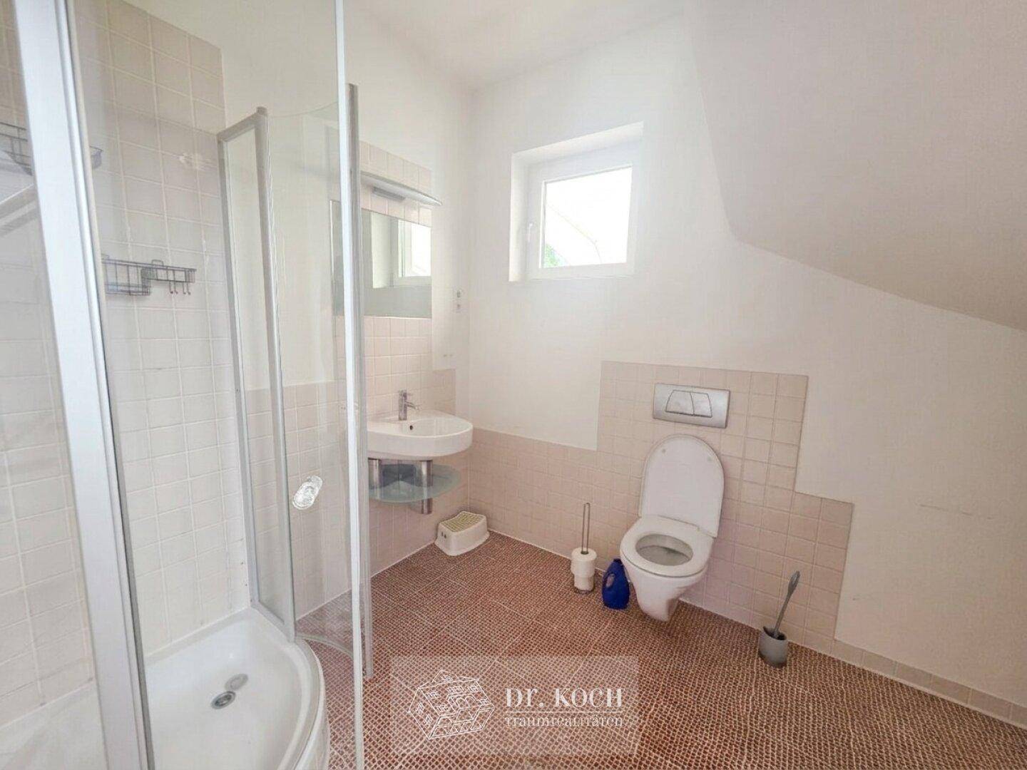 Badezimmer im Dachgeschoss mit Dusche, WC, Waschbecken und Fenster.