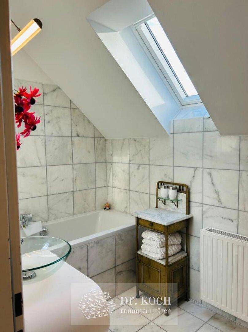Elegantes Badezimmer im Dachgeschoss mit Badewanne, Marmorfliesen und viel Tageslicht.