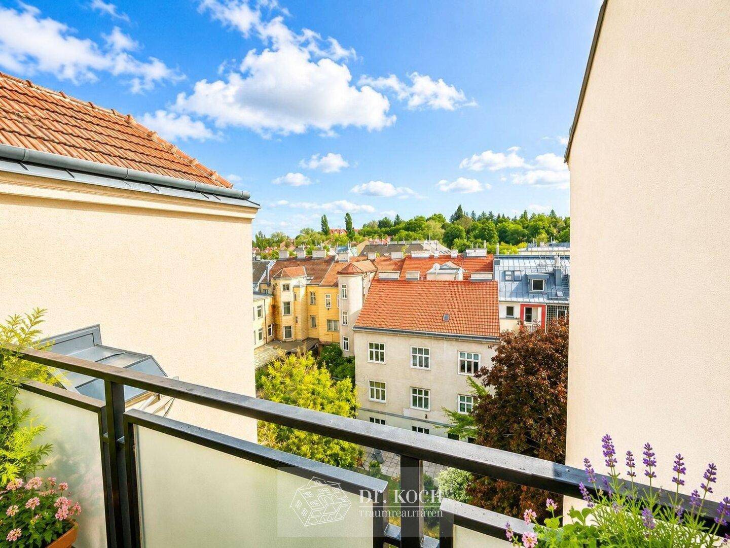 Panoramablick von einem Balkon über die umliegenden Dächer und grüne Baumwipfel.