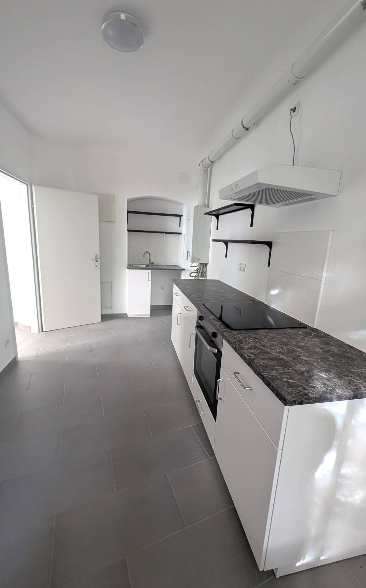 Moderne, helle Küche mit weißen Unterschränken, dunkler Arbeitsplatte und integriertem Kochfeld und Backofen.