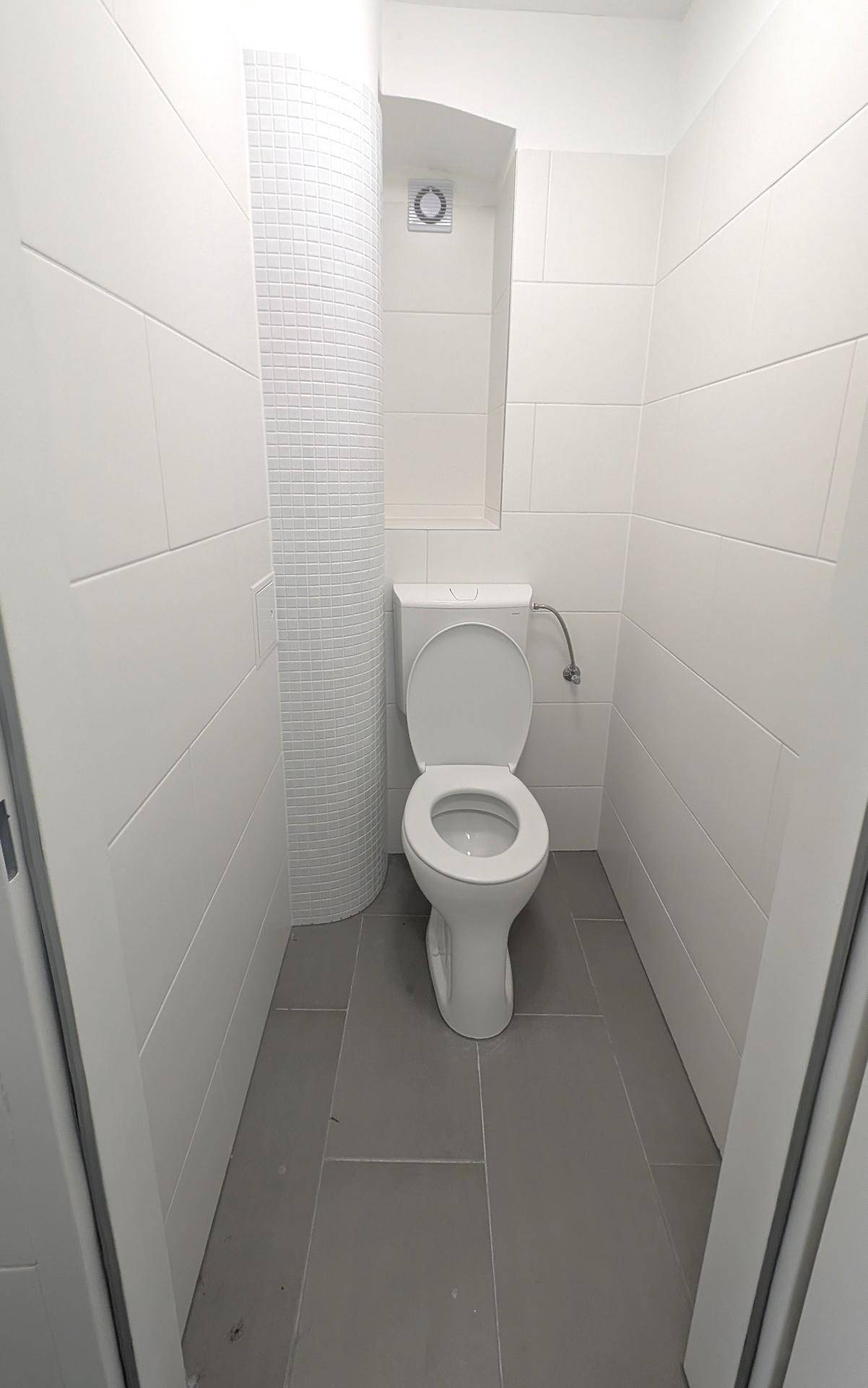 Kleines, hell gefliestes Gäste-WC mit Stand-WC und Abluftventilator an der Wand.
