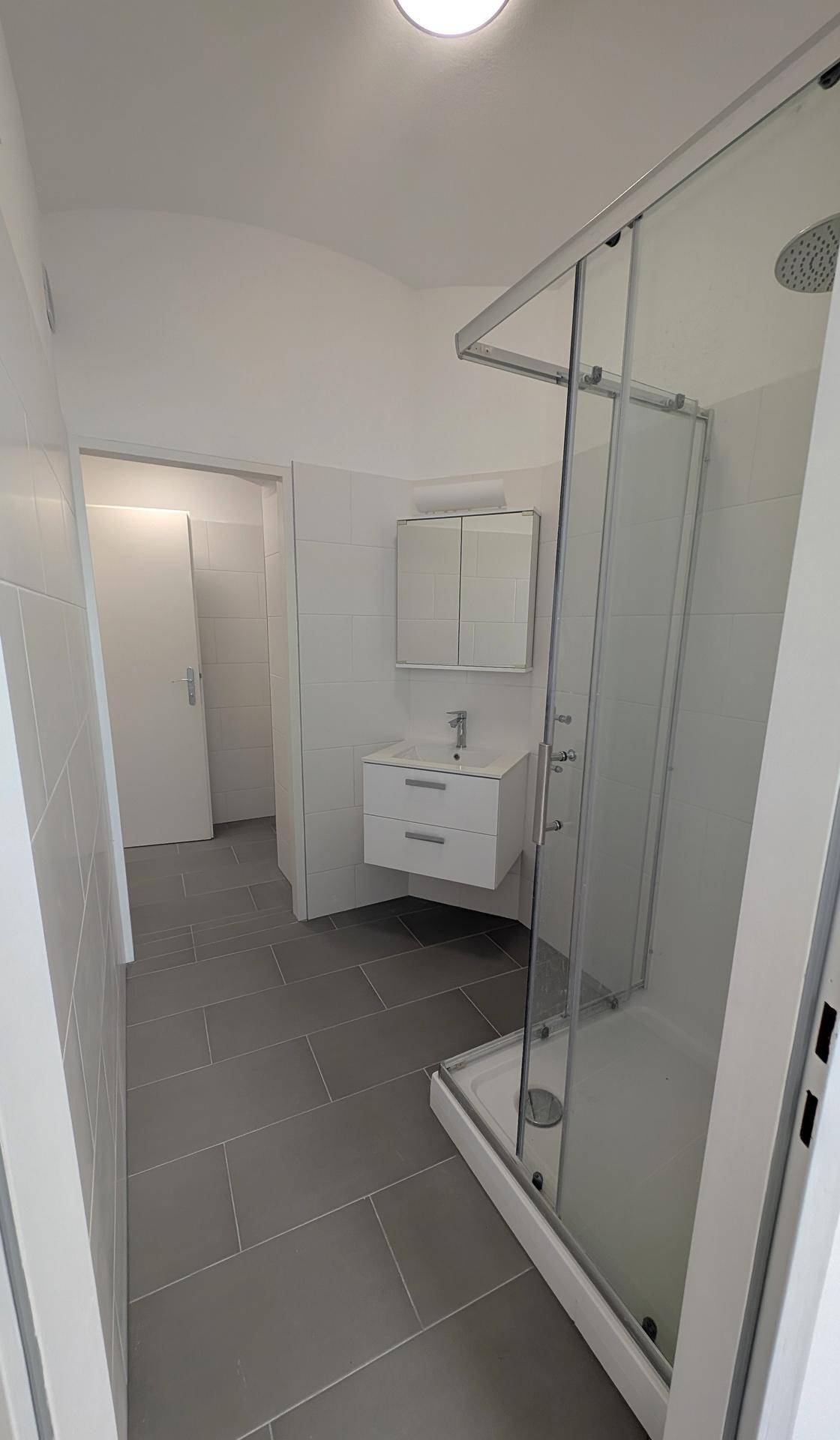 Modernes Badezimmer mit Duschkabine, weißem Waschtischunterschrank und grauen Bodenfliesen.