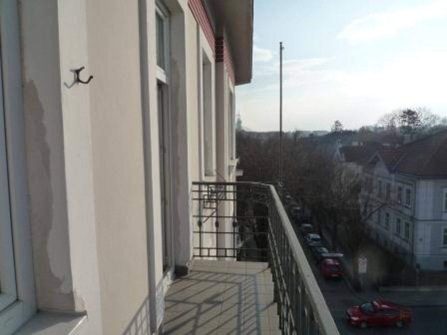 Balkon mit Metallgeländer und Blick auf die Straße sowie die umliegenden Gebäude.