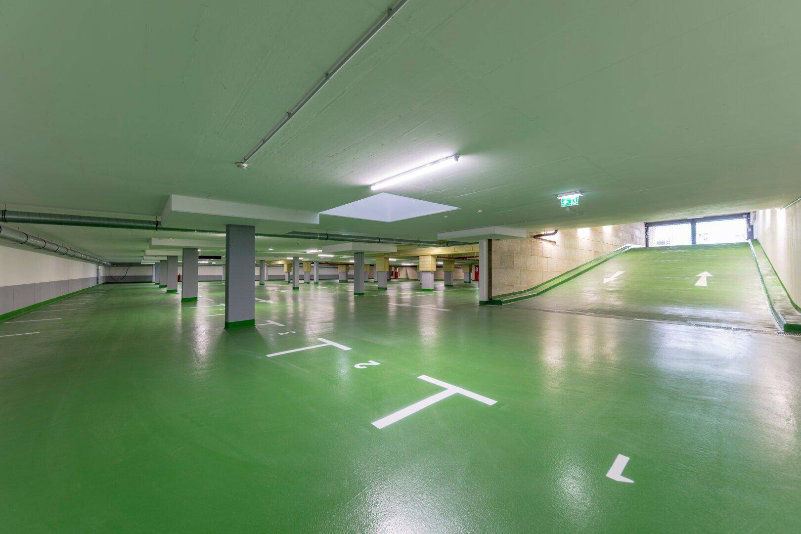 Geräumige Tiefgarage mit grüner Bodenmarkierung und breiter Zufahrtsrampe für Fahrzeuge.