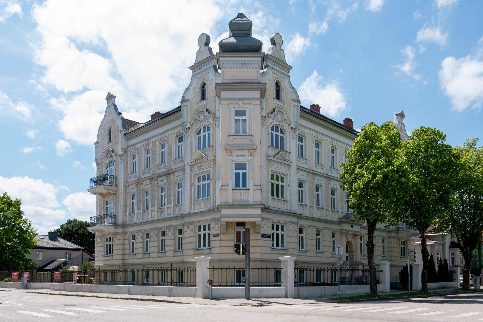 Prächtiges Eckgebäude im historischen Stil mit reich verzierten Fassaden und vielen Fenstern unter blauem Himmel.