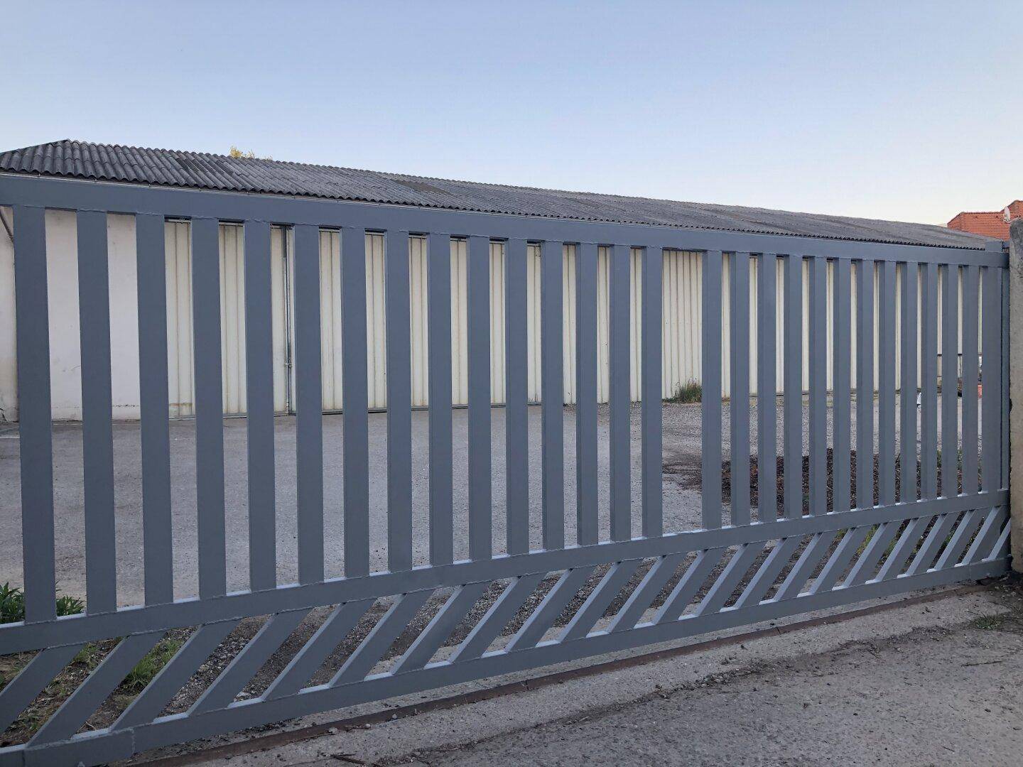 Modernes graues Metalltor mit vertikalen Lamellen und diagonalem Muster am unteren Rand.