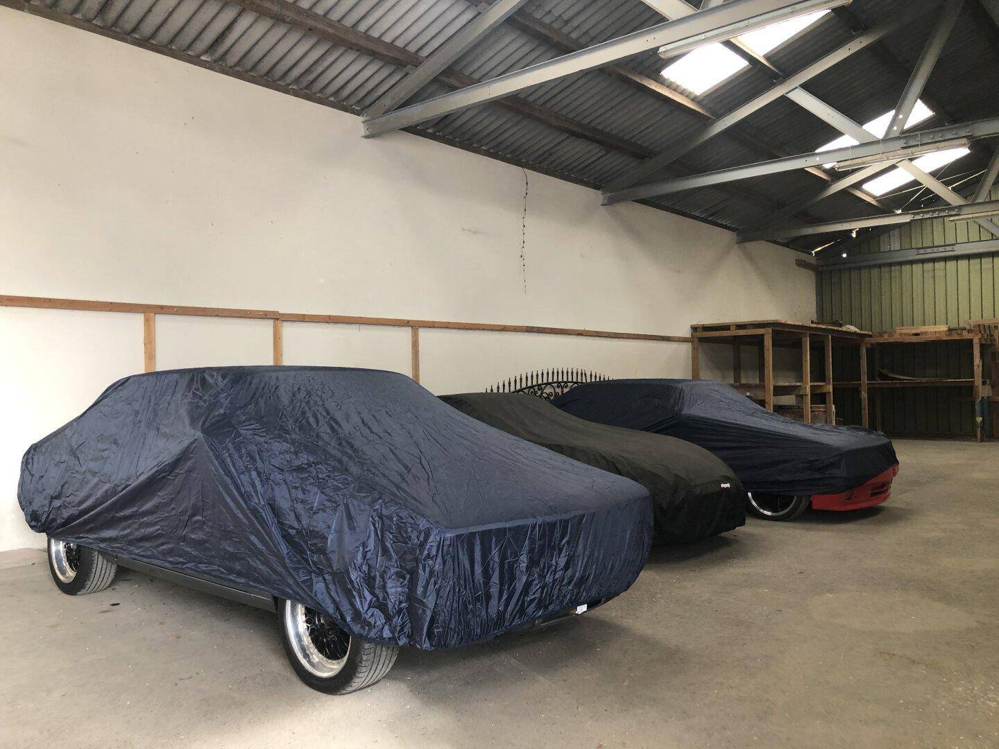 Geräumige Garage mit mehreren abgedeckten Fahrzeugen und sichtbarer Dachkonstruktion.