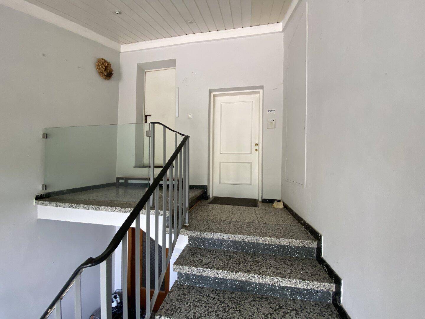 Treppenhaus mit Steinstufen, Metallgeländer und Glasbrüstung.