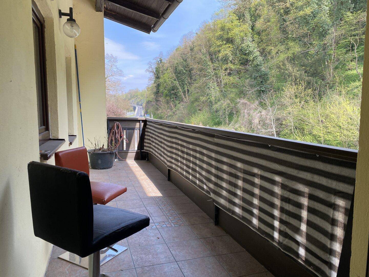 Kleiner Balkon mit Fliesenboden, Sitzgelegenheiten und Blick ins Grüne.