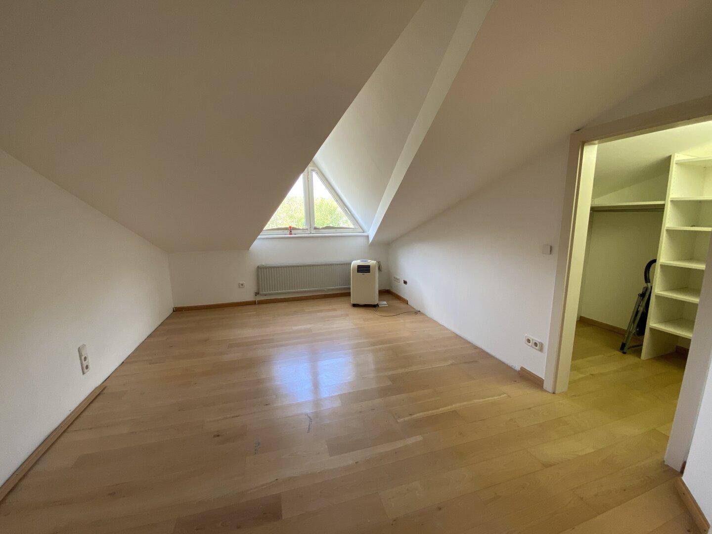 Geräumiges Schlafzimmer im Dachgeschoss mit Parkettboden und schrägem Fenster.