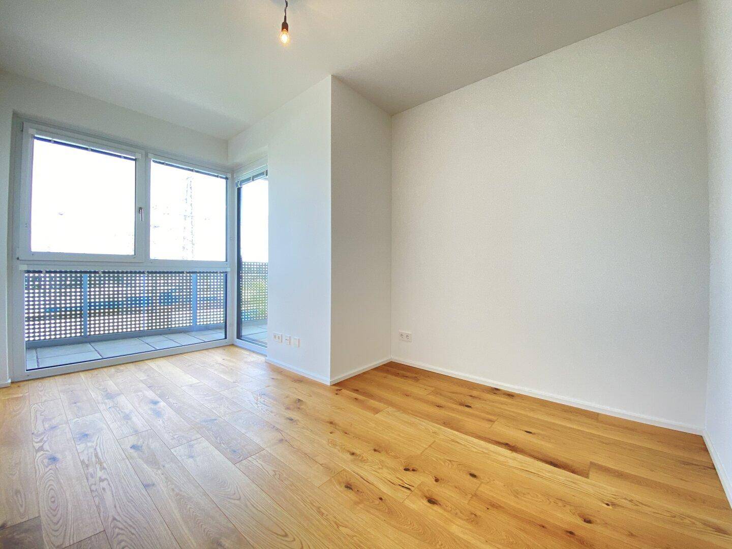 Geräumiger Raum mit Holzboden und Fensterfront, die einen Blick nach draußen ermöglicht.