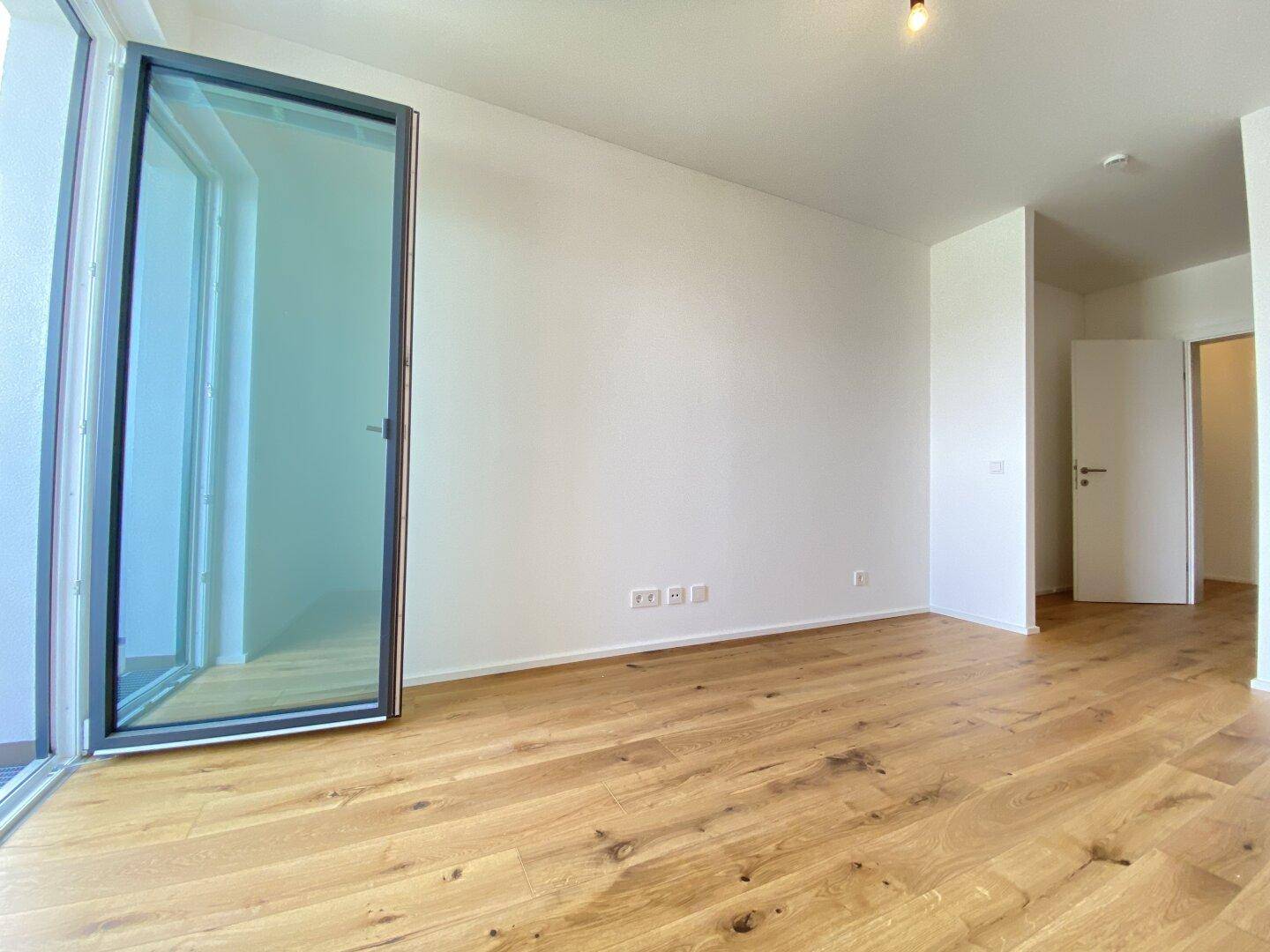 Unmöblierter Raum mit Holzboden und Zugang zu einem Balkon, bietet viel Gestaltungspotenzial.