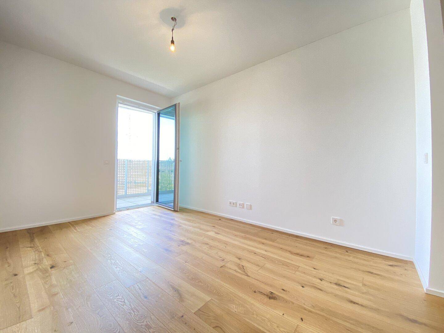 Lichtdurchfluteter Raum mit Holzboden und Balkonzugang, ideal für individuelle Nutzung.