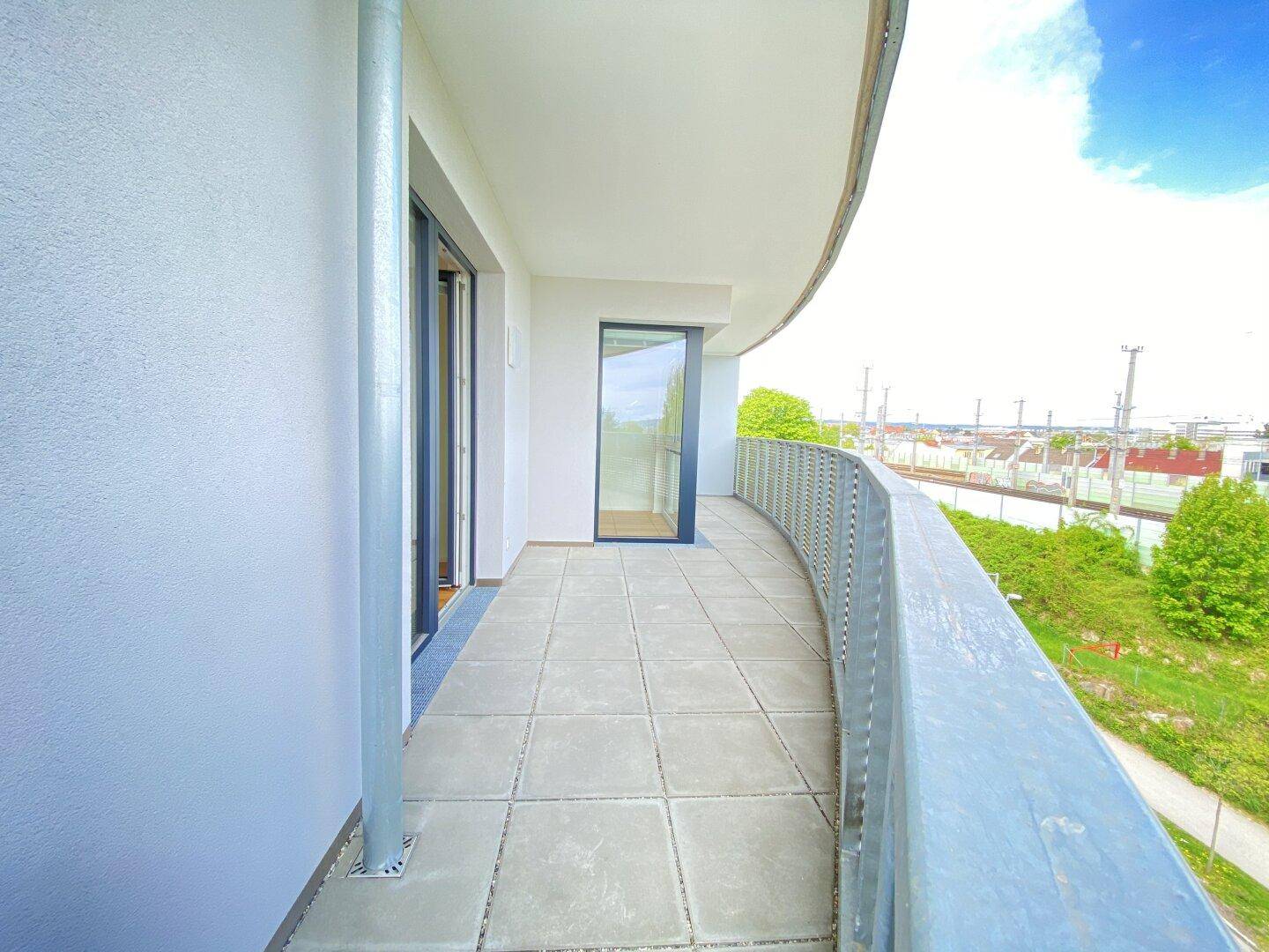 Langer, geschwungener Balkon mit Fliesenboden und Blick auf die Umgebung und Bahngleise.