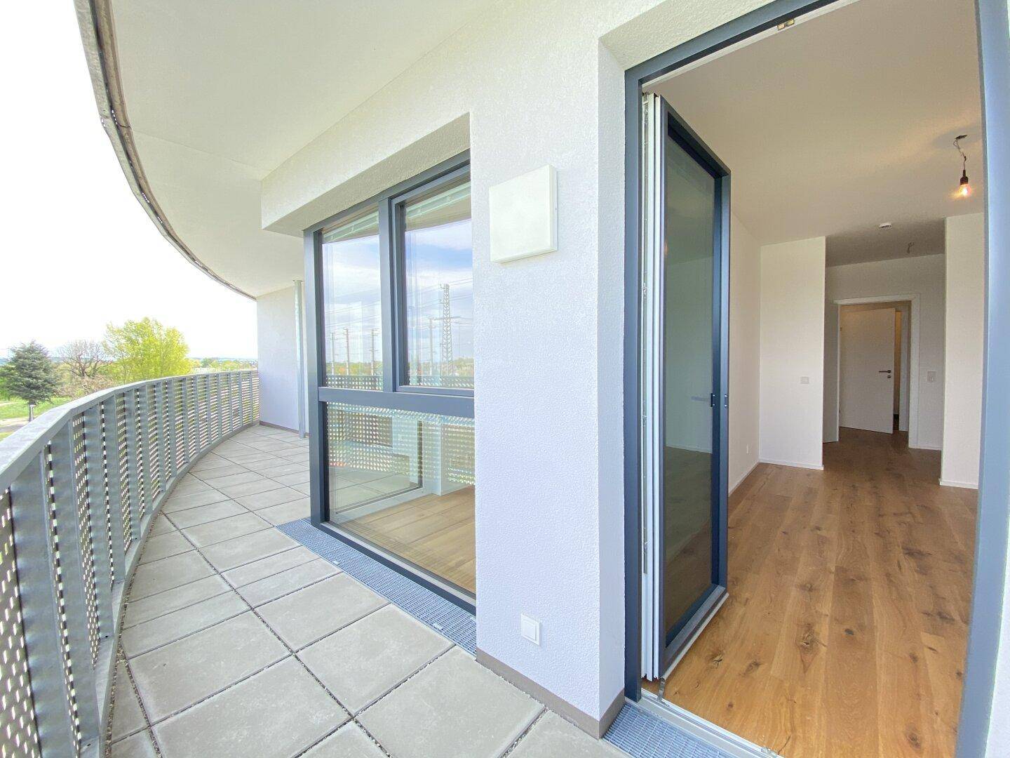 Geschwungener Balkon mit Fliesenboden und Metallgeländer, bietet Zugang zum Innenbereich.