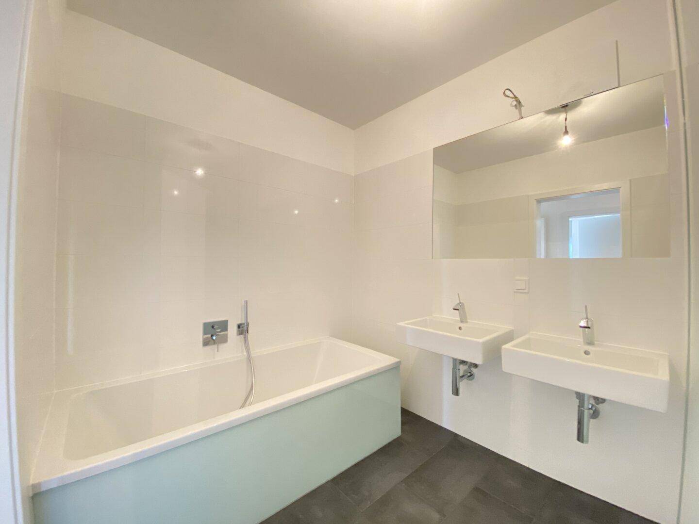 Helles Badezimmer mit Badewanne, zwei Waschbecken und großem Spiegel.