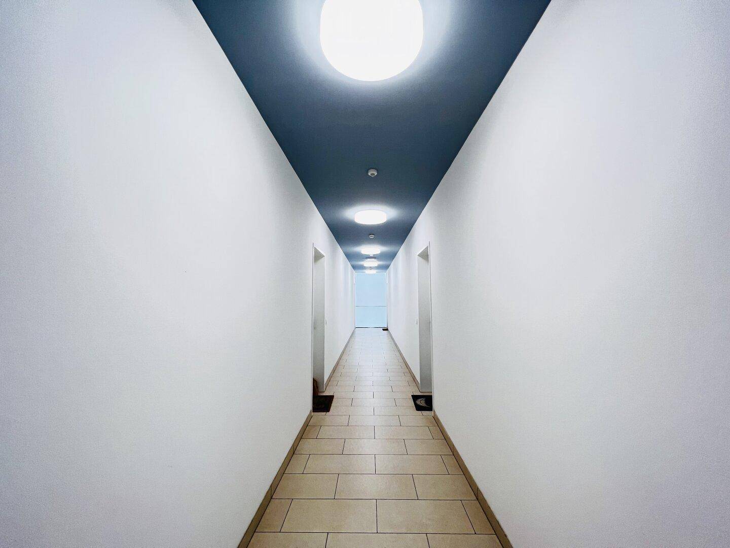 Langer Flur mit Fliesenboden und einer auffälligen dunkelblauen Decke mit Einbauleuchten.