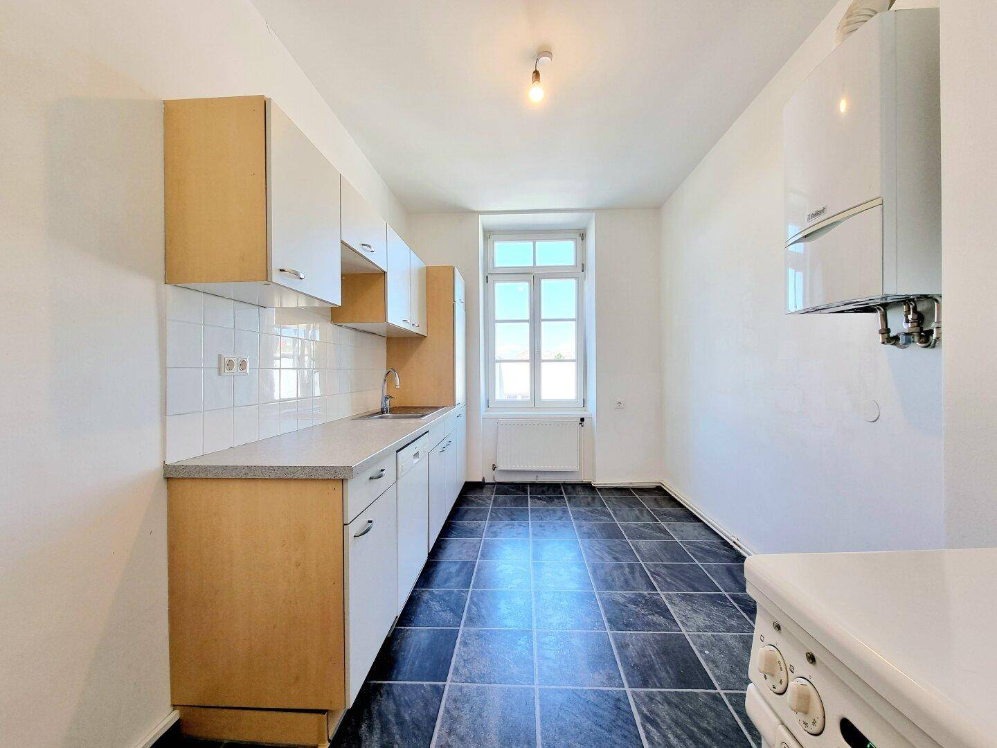 Funktionale Küche mit hellen Schränken, Fliesenboden und einem Fenster.
