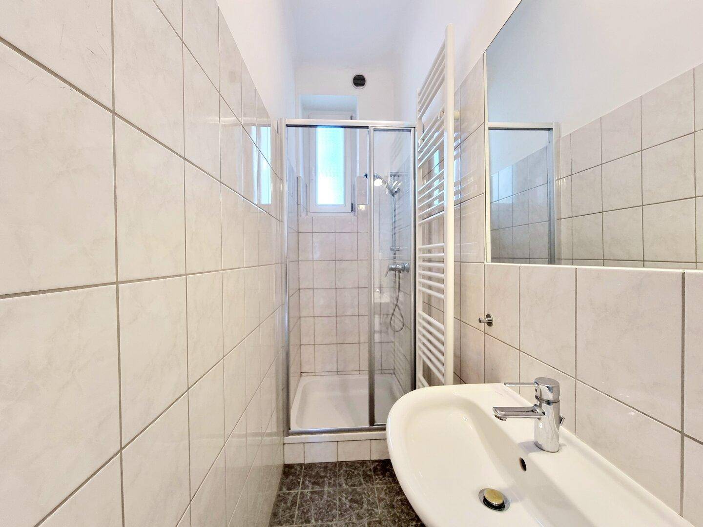 Modern gefliestes Badezimmer mit Duschkabine, Waschbecken und beheiztem Handtuchhalter.